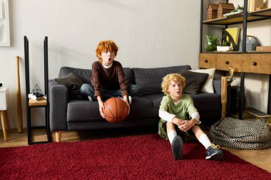İki heyecanlı çocuk rahat rahat evlerinde bir basketbol topuyla maç seyrediyor..