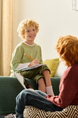 İki mutlu çocuk evde rahatlar, birlikte resim çizerken kahkaha ve yaratıcılıklarını paylaşırlar..