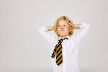 Sarışın bir çocuk okul üniforması ve çizgili kravat takarak rahatlıyor. Büyük hayaller kuruyor ve yanakları şişiriyor.