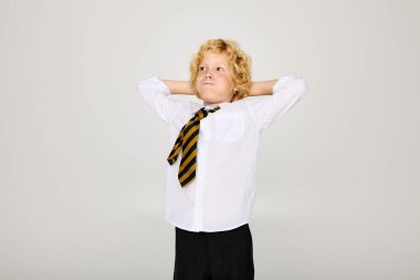 Dalgalı saçlı sarışın bir çocuk okul üniformasıyla gevşeyip yanaklarını şişiriyor.