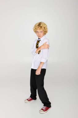 Dalgalı saçlı sarışın bir çocuk okul üniforması giyiyor ve stüdyoda neşeli bir poz veriyor..