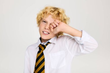 Okul üniforması giyen neşeli sarışın bir çocuk stüdyoda poz veriyor, neşeli bir ifade sergiliyor..