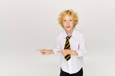 Okul üniformalı parlak gözlü çocuk, iyi ışıklandırılmış stüdyo alanını coşkuyla işaret ediyor..