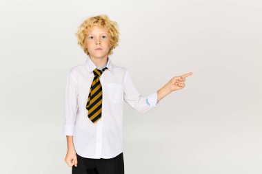 Dalgalı sarı saçlı genç bir çocuk stüdyoda duruyor okul üniforması ve çizgili kravat takıyor..