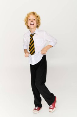 Okul üniformalı neşeli sarışın bir çocuk neşeli bir stüdyoda neşeyle dans ediyor..