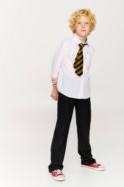 Sarı dalgalı saçlı çocuk okul üniforması giyiyor ve çizgili kravat takıyor. Stüdyoya güveni tam..