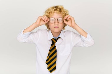 Okul üniformalı neşeli sarışın bir çocuk gözlüğünü neşeli bir ifadeyle ayarlıyor..