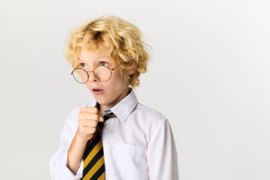 Okul üniformalı genç sarışın bir çocuk parlak bir stüdyoda şaşırmış görünüyor..