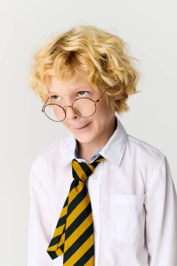 Sarışın, dalgalı saçlı, çizgili kravat ve gömlek giyen genç bir çocuk.