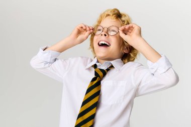 Okul üniformalı, gözlüklü ve çizgili kravatlı neşeli bir sarışın çocuk neşeyle gülüyor..