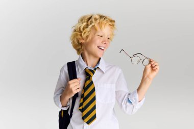 Dalgalı sarı saçlı, çizgili kravat takan ve mutlu bir şekilde gülümseyen bir okul çocuğu..