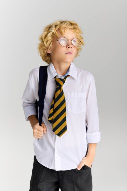 Dalgalı sarı saçlı genç bir çocuk okul üniforması giyiyor ve düşünceli bir şekilde stüdyoda görünüyor..