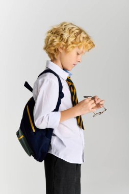 Dalgalı saçlı genç bir sarışın okul üniforması giyerken gözlüğünü düzeltiyor..