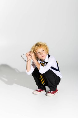 Dalgalı sarı saçlı, düşünceli, okul üniforması ve kravatı olan genç bir çocuk..