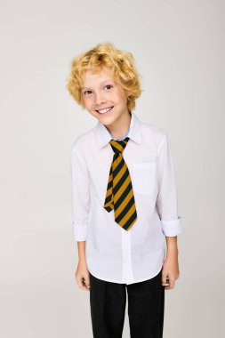 Okul üniformalı neşeli sarışın bir çocuk stüdyoda çizgili bir kravat takıyor..