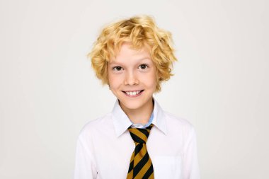 Okul üniformalı neşeli bir sarışın stüdyoda güvenle duruyor ve mutluluk saçıyor..