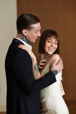 Sıcak bir otel odasında genç bir çift gülümsüyor ve nazikçe sarılıyor..