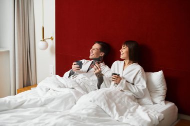 Genç bir çift yatağa oturur, bornozlara bürünür, sıcak içkileri ve kahkahaları paylaşır, mutluluğu tadarlar..