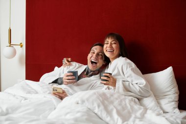 Beyaz cüppeli çift sıcak bir otel ortamında sarılırken kahkahalar ve içkileri paylaşıyor..