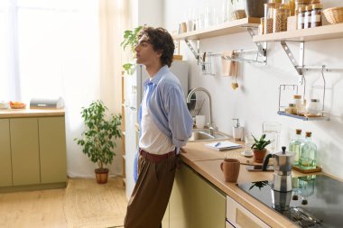 Genç bir ortadoğulu adam modern mutfağında rahatça duruyor ve çevresinin tadını çıkarıyor..