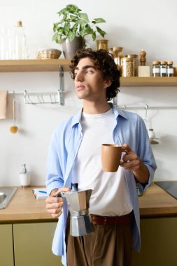 Kıvırcık saçlı yakışıklı genç adam evde rahatlıyor, mutfakta sıcak bir içkinin tadını çıkarıyor..