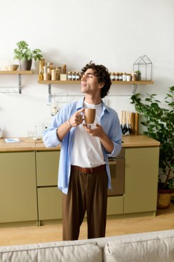 Orta Doğulu genç bir adam kıvırcık saçlı evde rahatlıyor, kahvesinin tadını çıkarıyor..