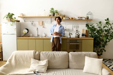 Genç bir ortadoğulu adam evinde dinleniyor, şık bir mutfakta bir bardak tutuyor..