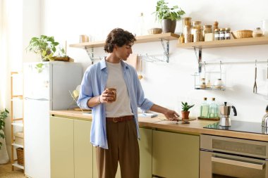 Kıvırcık saçlı genç bir adam evinde bir bitkiyle ilgilenirken sakin bir anın tadını çıkarıyor..