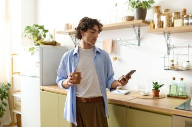 Kıvırcık saçlı genç bir ortadoğulu elinde fincanla, rahat bir mutfakta telefonuyla meşgul..