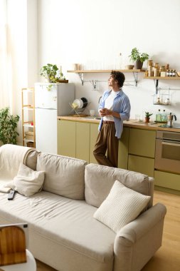 Kıvırcık saçlı genç adam rahat dairesinde rahatlar, bir yudum içer ve hayal kurar..