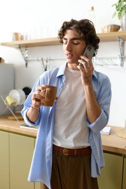 Kıvırcık saçlı yakışıklı bir adam dairesinde telefonla konuşurken kahvesini yudumluyor..