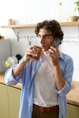 Kıvırcık saçlı, kahvesini yudumlayan ve rahat dairesinde telefonla konuşan genç bir adam..