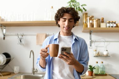 Yakışıklı genç adam dairesinde bir fincan kahveyle rahatlar, telefonuyla meşgul olur..