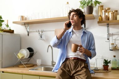 Kıvırcık saçlı genç adam telefonda konuşurken şık dairesinde rahatlıyor..