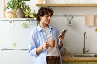 Kıvırcık saçlı genç bir adam evde rahatlıyor, kahvesini yudumluyor ve telefonunu karıştırıyor..