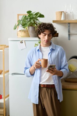 Genç bir ortadoğulu adam dairesinde dinleniyor, telefonunu kontrol ederken çay içiyor..