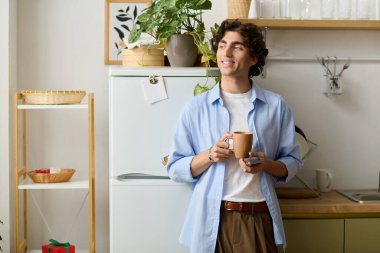 Kıvırcık saçlı yakışıklı bir genç adam elinde bir bardak tutarken evinde rahatlıyor, mutlu görünüyor..