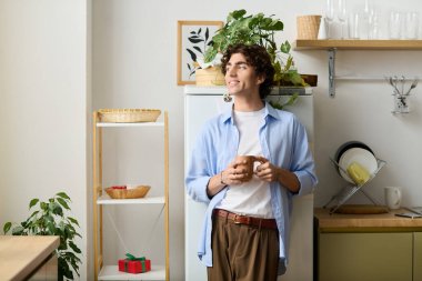 Dairesinde kıvırcık saçlı genç bir adam elinde ılık bir içecek ve gülümsüyor..