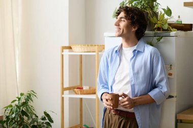 Kıvırcık saçlı yakışıklı genç adam dairesinde rahatlıyor, sıcak bir içki içiyor ve gülümsüyor..