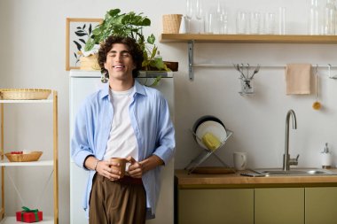 Genç, orta doğulu kıvırcık saçlı bir adam sıcacık mutfağında duruyor ve gülümsüyor..