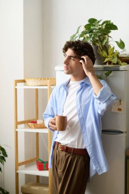 Kıvırcık saçlı genç adam evde gevşiyor. Etrafı yeşilliklerle çevriliyken sıcak bir içecek yudumluyor..