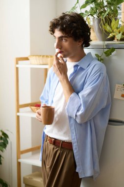 Genç bir adam evinde çay yudumlarken dinleniyor, düşüncelere dalmış ve anın tadını çıkarıyor..