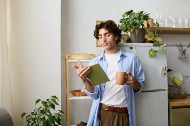 Genç adam şık dairesinde rahatlar, kitap okurken kahvesini yudumlar.