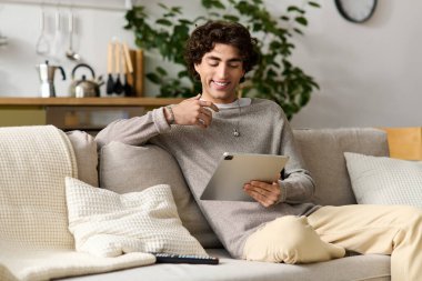 Neşeli genç adam evde vakit geçirmeyi seviyor, rahat bir duruşu olan tablet üzerinde geziniyor..