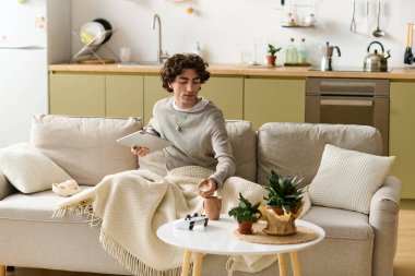 Kıvırcık saçlı genç bir adam dairesinde bitkilerle çevrili huzurlu bir anın tadını çıkarıyor..