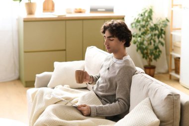 Yakışıklı genç bir adam kanepede rahat rahat sıcak içkisini yudumluyor..