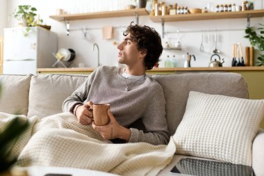 Kıvırcık saçlı genç bir orta doğulu kanepeye oturmuş sıcak içkisinin tadını çıkarıyor..