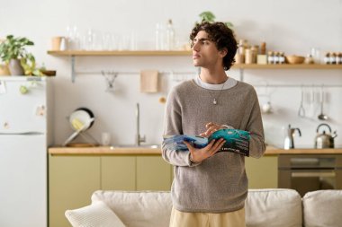 Kıvırcık saçlı adam evde rahatlıyor, rahat bir atmosferle çevrili iken dergi okuyor..