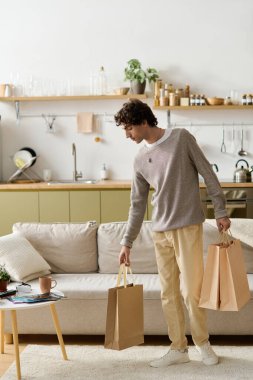 Kıvırcık saçlı genç bir ortadoğulu, alışveriş çantalarını açarken evde dinlenmekten zevk alıyor..