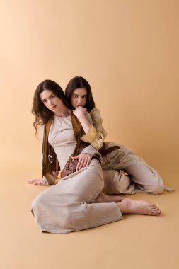 Güzel genç ikiz kız kardeşler birlikte sanatsal poz verirken şık kıyafetlerini sergilerler..